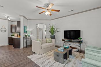 A living room with plank flooring, a ceiling fan, crown molded ceilings, and an arched doorway.